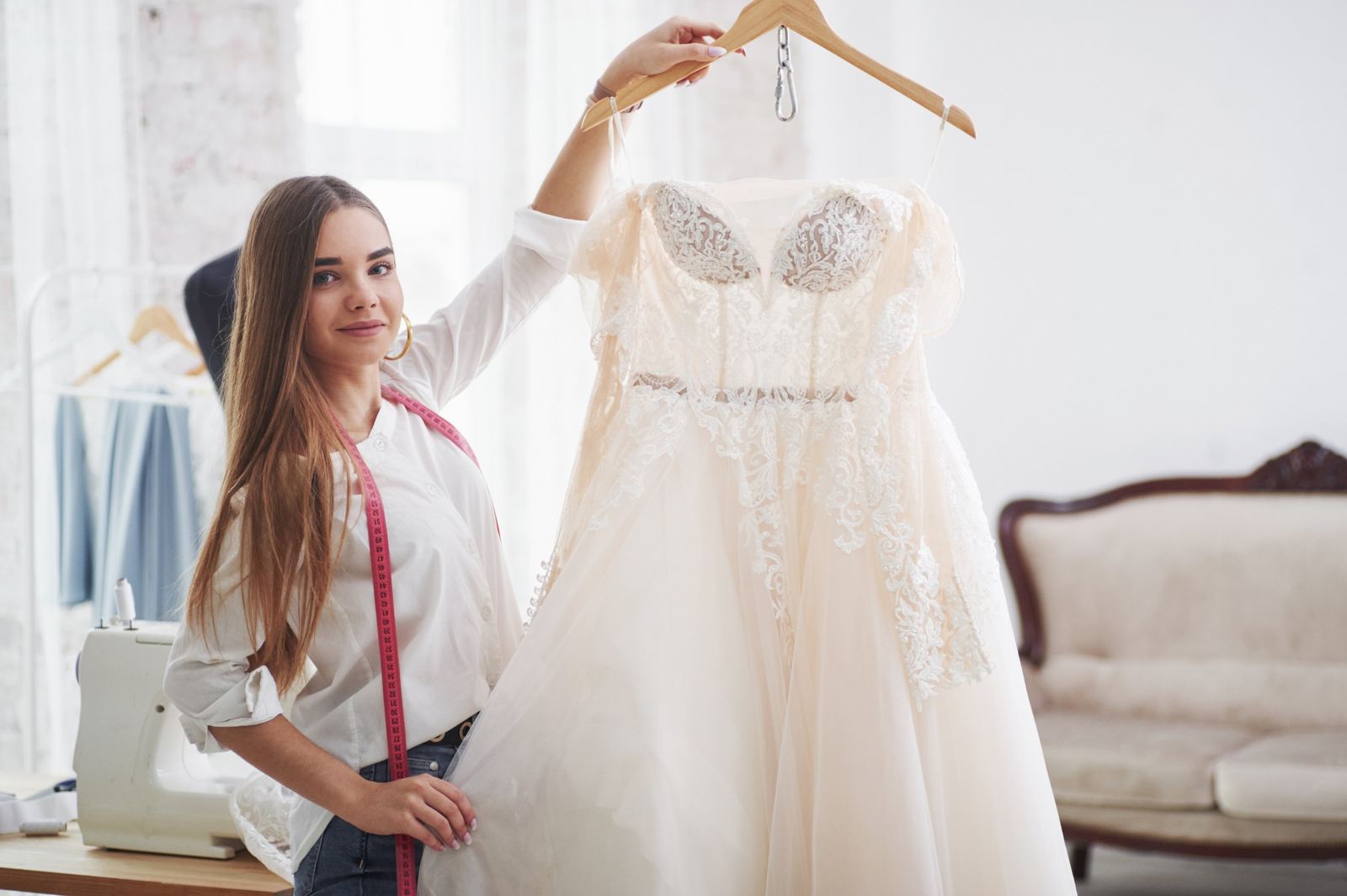 Seamstress holding a lace wedding dress on a hanger